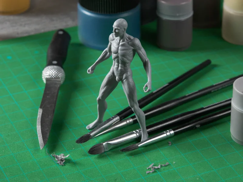 Miniaturenset auf grüner Schneidematte mit Figuren, feinen Pinseln und Bastelmesser